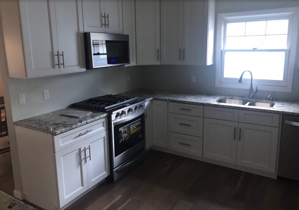 Modern kitchen renovation in a Jersey Shore home featuring white shaker cabinets, granite countertops, stainless steel appliances, and new wood flooring installed by GYB Construction.