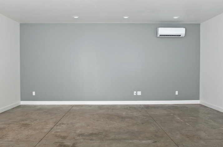 Finished garage conversion with smooth concrete floor, gray painted accent wall, recessed ceiling lights, and a mounted mini-split HVAC unit.